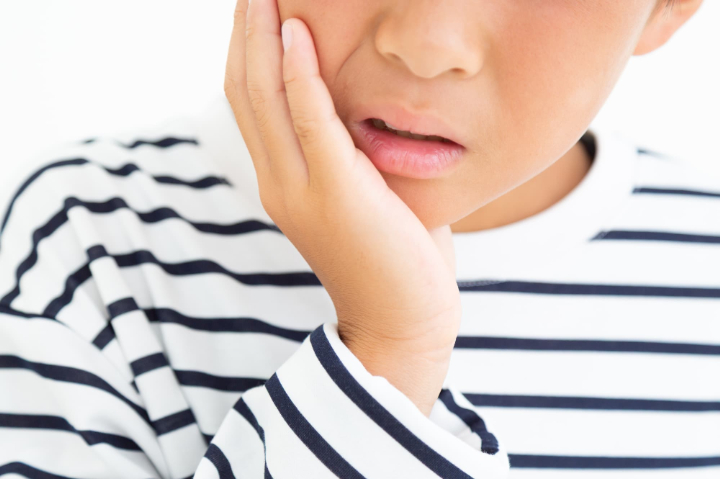 痛そうに頬を押さえる子ども