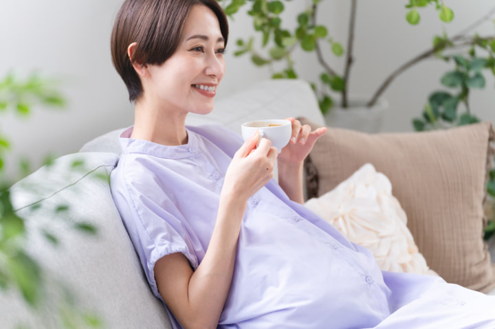 ソファで飲み物を飲んでくつろいでいる妊婦